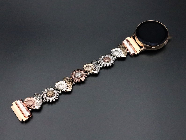 May include: A gold, silver, and rose gold watch band with a sunflower design. The band is made of metal and has a clasp closure.