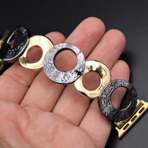 May include: A black and gold metal watch band with a textured, circular design. The band is made up of multiple interlocking circles.