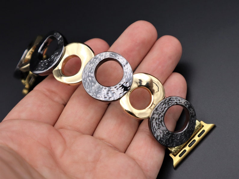 May include: A black and gold metal watch band with a textured, circular design. The band is made up of multiple interlocking circles.
