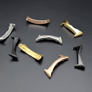 May include: A collection of metal watch band links in various colors, including silver, gold, black, and rose gold. The links have a curved design and are arranged on a dark surface. The variety of finishes suggests options for watch customization.