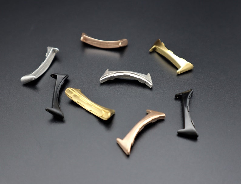 May include: A set of eight metal watch band spring bars in different colors, including black, gold, and silver. The spring bars are designed to connect watch bands to watch cases.