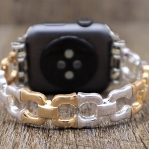 May include: A two-tone watch band with a chain link design. The links alternate between gold and silver colors. The watch band is attached to a black smartwatch.