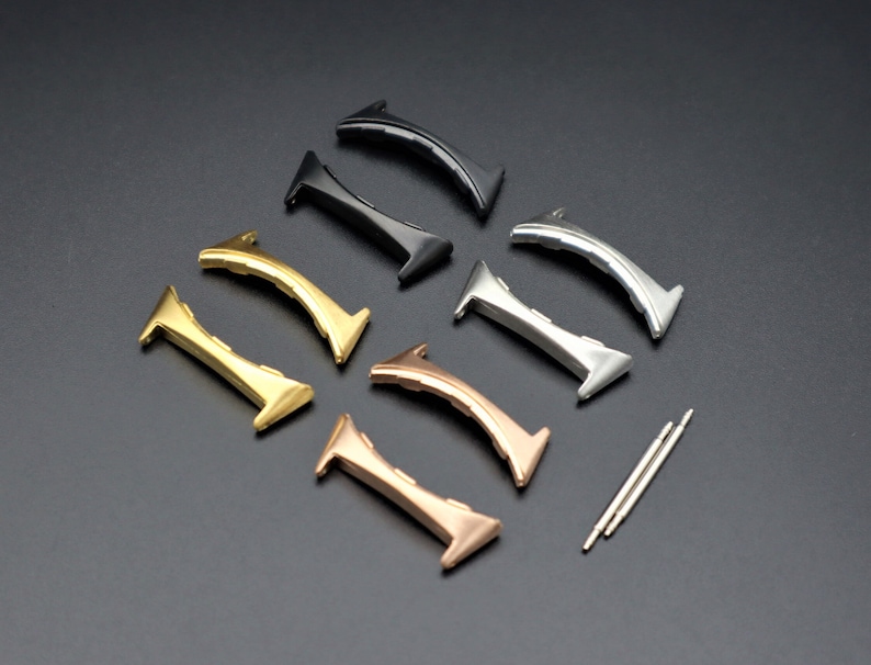 May include: Seven watch band spring bars in different colors: gold, rose gold, silver, and black. The spring bars are arranged in a semi-circle on a black surface.