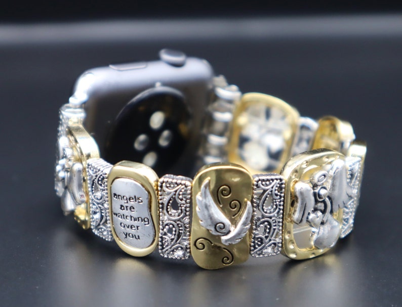 May include: A gold and silver watch band with a charm bracelet style. The charms feature angels, wings, and the text "angels are watching over you".