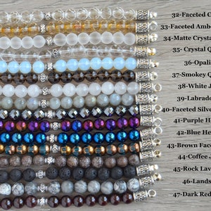 May include: A collection of 15 different gemstone bracelets with silver clasps. The bracelets are arranged vertically from top to bottom, with the names of each gemstone listed to the right of the image. The gemstones include faceted crystal, amber crystal, matte crystal quartz, crystal quartz, opalite, smokey quartz, white jade, labradorite, faceted silver hematite, purple hematite, blue hematite, brown faceted aqua, coffee jasper, rock lava beads, landscape, and dark red garnet.