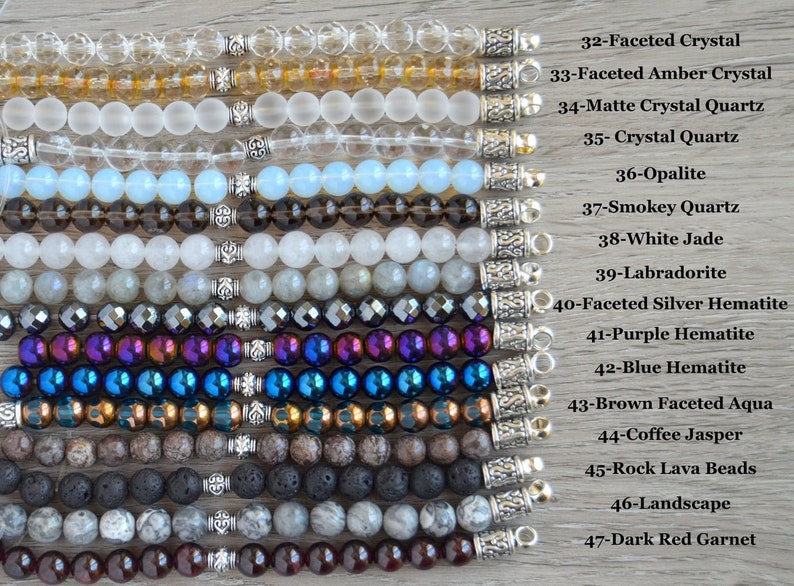 May include: A collection of 15 different gemstone bracelets with silver clasps. The bracelets are arranged vertically from top to bottom, with the names of each gemstone listed to the right of the image. The gemstones include faceted crystal, amber crystal, matte crystal quartz, crystal quartz, opalite, smokey quartz, white jade, labradorite, faceted silver hematite, purple hematite, blue hematite, brown faceted aqua, coffee jasper, rock lava beads, landscape, and dark red garnet.