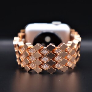 May include: A rose gold Apple Watch band with a diamond-like pattern. The band is made of metal links and has a clasp closure.