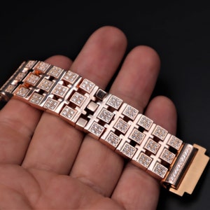 May include: Rose gold watch strap with square diamond detailing. The strap is composed of interconnected rectangular links, each set with small diamonds. The clasp also features a row of diamonds.