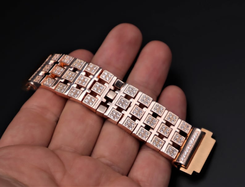 May include: Rose gold watch strap with square diamond detailing. The strap is composed of interconnected rectangular links, each set with small diamonds. The clasp also features a row of diamonds.