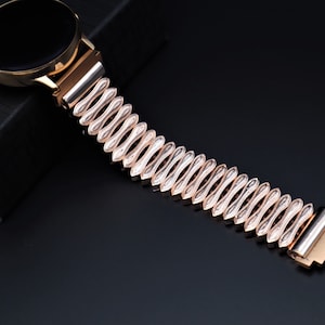 K&ouml;nnte beinhalten: Ein ros&eacute;goldenes Metallarmband mit einem einzigartigen wellenf&ouml;rmigen Design. Das Armband besteht aus miteinander verbundenen, ovalen Teilen.