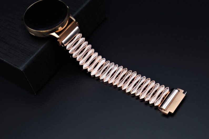 K&ouml;nnte beinhalten: Ein ros&eacute;goldenes Metallarmband mit einem einzigartigen wellenf&ouml;rmigen Design. Das Armband besteht aus miteinander verbundenen, ovalen Teilen.