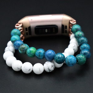 May include: A rose gold fitness tracker with a white and blue beaded bracelet. The bracelet is made of two strands of beads, one white and one blue.