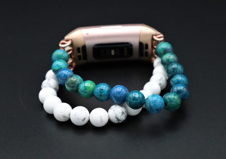 May include: A rose gold fitness tracker with a white and blue beaded bracelet. The bracelet is made of two strands of beads, one white and one blue.