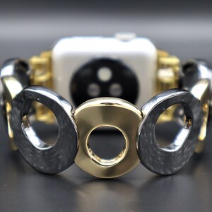 May include: A gold and silver watch band with a circular design. The band is made of metal and has a textured finish.