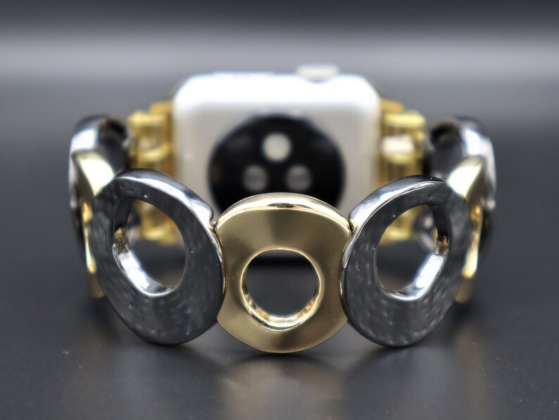 May include: A gold and silver watch band with a circular design. The band is made of metal and has a textured finish.