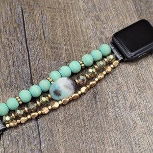 May include: A turquoise and gold beaded Apple Watch band with a large, oval-shaped gemstone. The band is made of wooden beads, gold beads, and clear crystal beads.