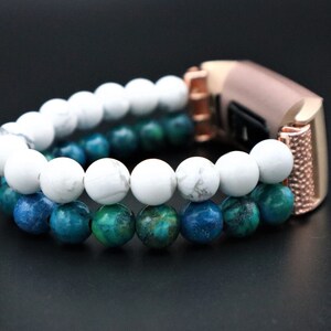 May include: A rose gold fitness tracker band with a double row of beads. The top row is white and the bottom row is blue and green.