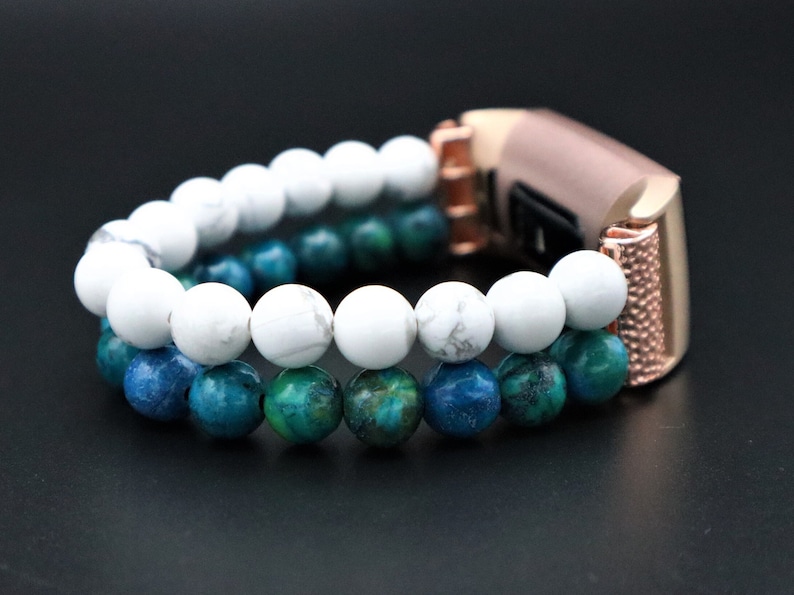 May include: A rose gold fitness tracker band with a double row of beads. The top row is white and the bottom row is blue and green.