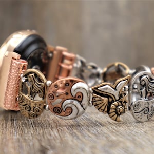 May include: A rose gold smartwatch with a decorative metal band featuring a mermaid, waves, and a bird design. The band is made of mixed metals with silver, gold, and copper tones.