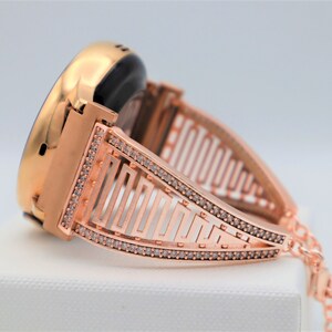 May include: Rose gold smartwatch band with a geometric design and clear rhinestones.