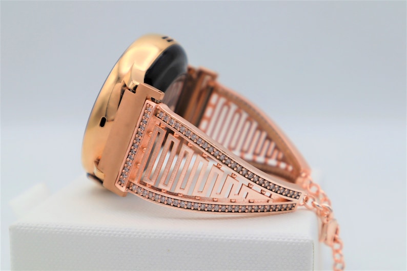 May include: Rose gold smartwatch band with a geometric design and clear rhinestones.