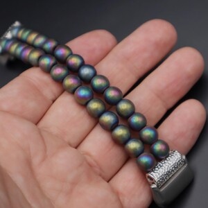 May include: A double-row bracelet made of iridescent, dark grey beads with a silver clasp.
