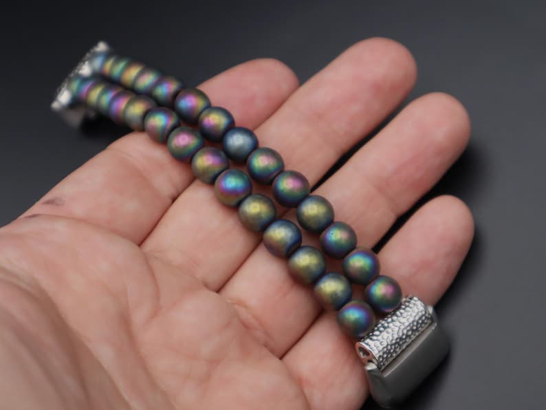 May include: A double-row bracelet made of iridescent, dark grey beads with a silver clasp.