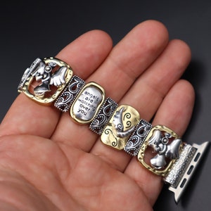 May include: A silver and gold watch band with a decorative design featuring angels and the text "angels are watching over you".