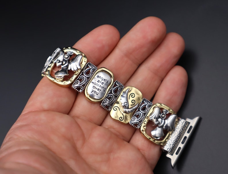 May include: A silver and gold watch band with a decorative design featuring angels and the text "angels are watching over you".