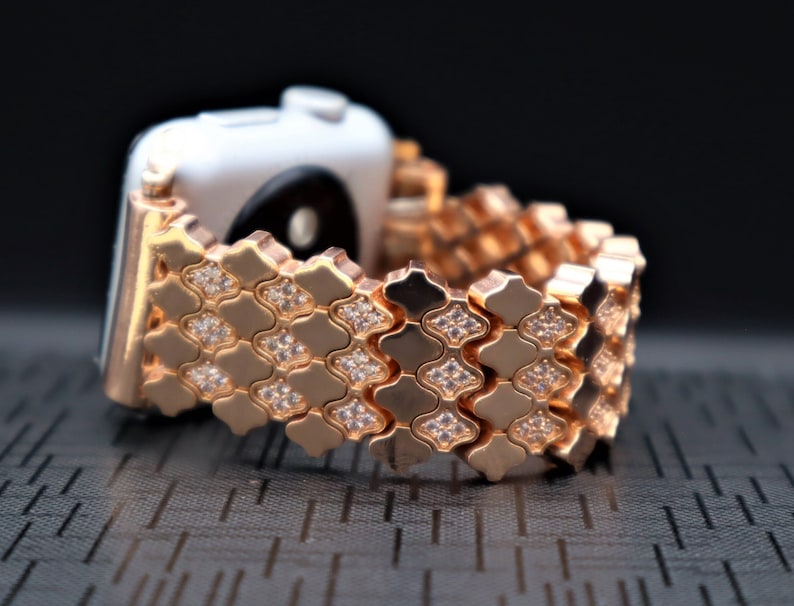 May include: Rose gold Apple Watch band with a diamond-like pattern. The band is made of metal and has a shiny finish.