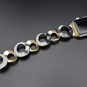 May include: A gold and black watch band with a chain-link design. The band is made of metal and has a textured finish.
