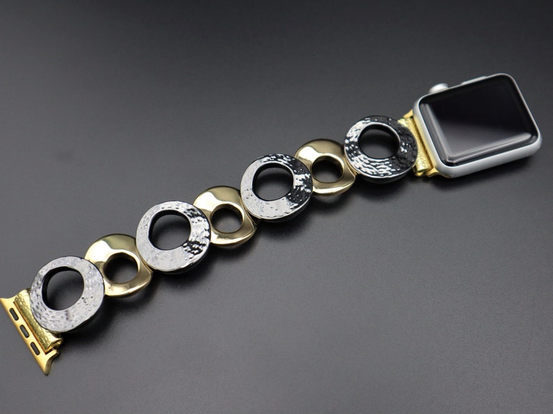 May include: A gold and black watch band with a chain-link design. The band is made of metal and has a textured finish.