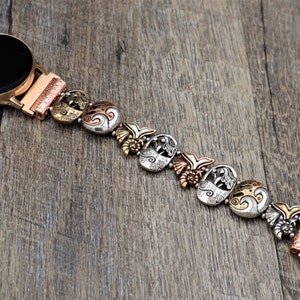 May include: A silver and copper watch band with a mermaid design. The band is made up of multiple charms with intricate details.
