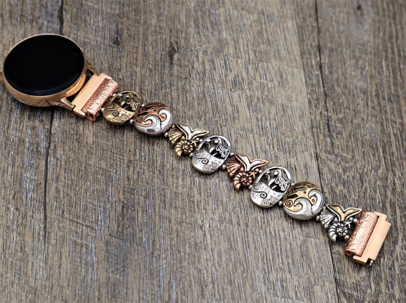 May include: A silver and copper watch band with a mermaid design. The band is made up of multiple charms with intricate details.