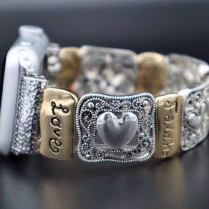May include: Silver and gold Apple Watch band with a heart charm and engraved words "Love" and "Faith".