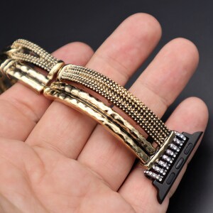 May include: A gold and black watch band with a textured design and rhinestones. The band is made of metal and has a clasp closure.