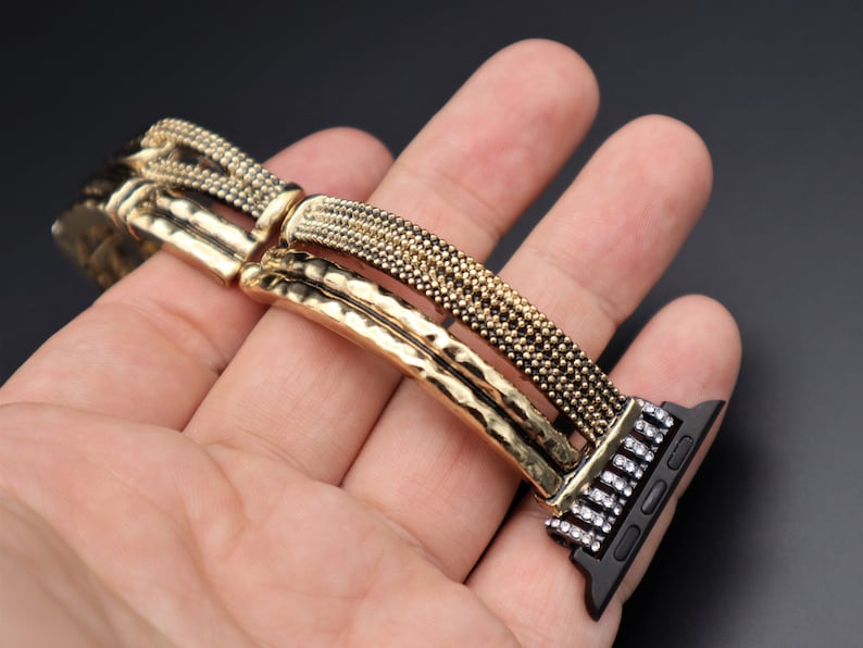May include: A gold and black watch band with a textured design and rhinestones. The band is made of metal and has a clasp closure.