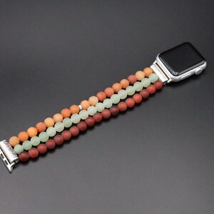 May include: A three-strand beaded Apple Watch band with red, green, and orange beads. The band is made of smooth, round beads and has a silver clasp.