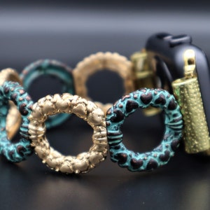 Puede incluir: Una pulsera de reloj de color dorado y turquesa hecha de círculos unidos. La pulsera está diseñada para adaptarse a un Apple Watch.