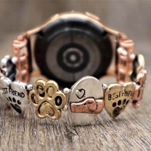 Puede incluir: Correa de reloj decorativa con huellas de patas, corazones y la inscripci&oacute;n "BEST FRIEND". La correa tiene una mezcla de tonos plateados, dorados y cobrizos. El reloj tiene un acabado en oro rosa.