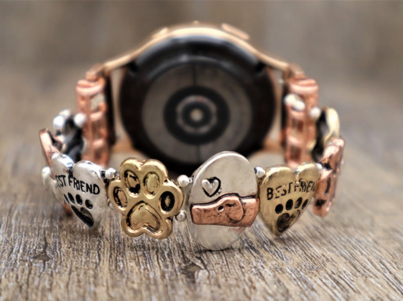 Puede incluir: Correa de reloj decorativa con huellas de patas, corazones y la inscripci&oacute;n "BEST FRIEND". La correa tiene una mezcla de tonos plateados, dorados y cobrizos. El reloj tiene un acabado en oro rosa.