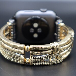 May include: Gold-toned watch band with a textured, hammered metal design. The band has a decorative, intricate pattern with small beads and a clasp closure.