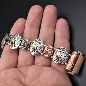 Pode incluir: Um bracelete de prata e cobre com um design floral e detalhes de borboleta. O bracelete tem um fecho de encaixe.