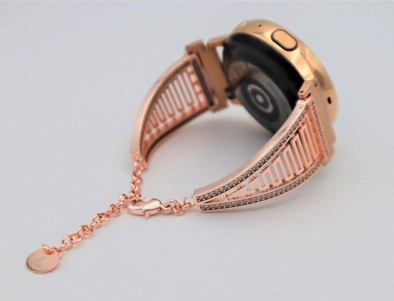 May include: Rose gold watch band with a geometric design and a diamond-like finish. The band is made of metal and has a clasp closure.