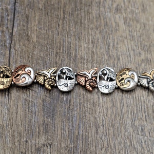 May include: A silver and copper bracelet with a mermaid and wave design. The bracelet is made of metal and has a clasp closure.