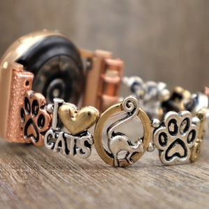 May include: A rose gold smartwatch with a charm bracelet attachment. The charms include paw prints, a heart with "I love cats" written on it, a cat, and more paw prints.