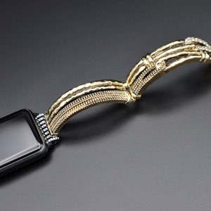 May include: A gold-toned watch band with a textured design and clear rhinestones. The band is designed to fit a smart watch.