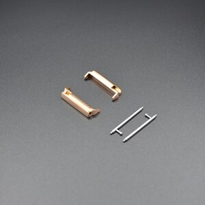 May include: Two gold-colored metal watch band connectors and two silver-colored metal spring bars.