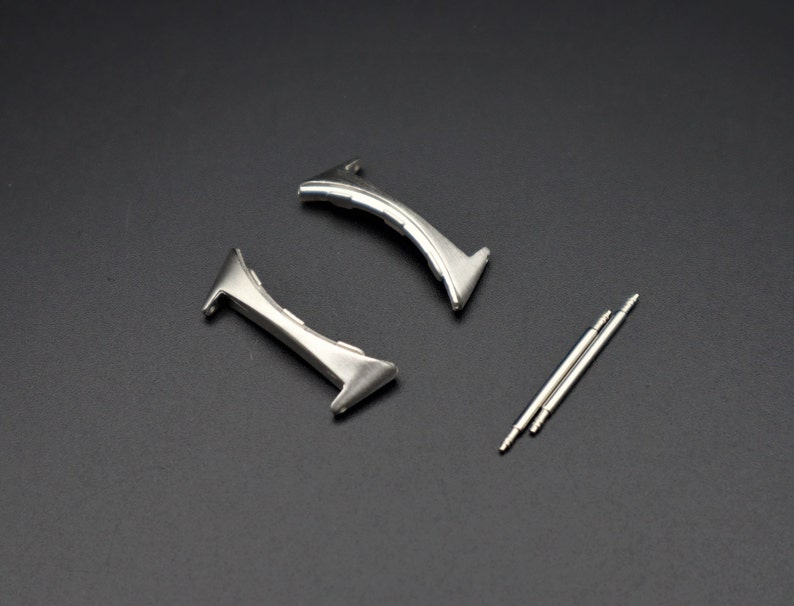 May include: Two silver watch band spring bars and two silver watch band clasps.