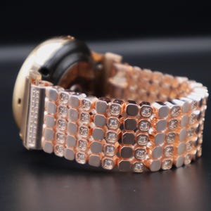 May include: A rose gold smartwatch with a diamond-encrusted band. The band is made up of multiple rows of small, square-shaped links, each with a single diamond set in the center.